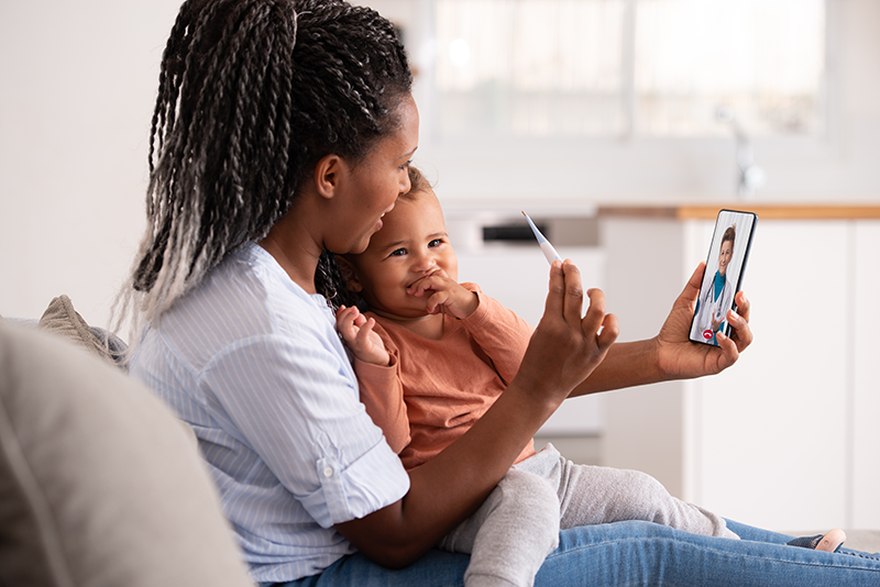 A woman with a baby and thermometer talking to a doctor through video call.