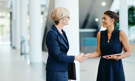 Two professional women smiling and shaking hands.