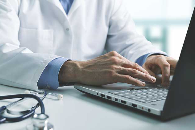 Doctor typing on a laptop at a desk.