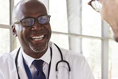 A doctor with glasses, smiling and talking to a person in the foreground.